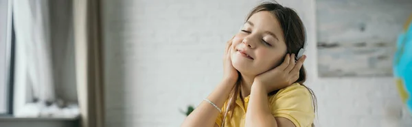 Happy preteen girl with closed eyes listening music in headphones at home, banner — Stock Photo