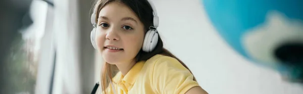 Chica sonriente mirando a la cámara mientras escucha música en los auriculares, pancarta - foto de stock
