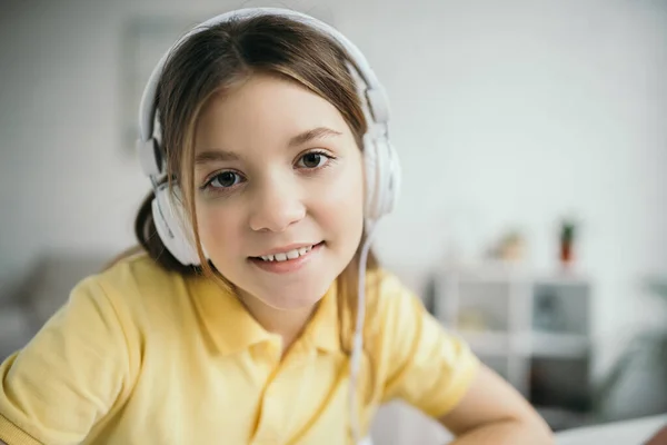 Retrato de niña preadolescente feliz escuchando música en los auriculares y sonriendo a la cámara - foto de stock