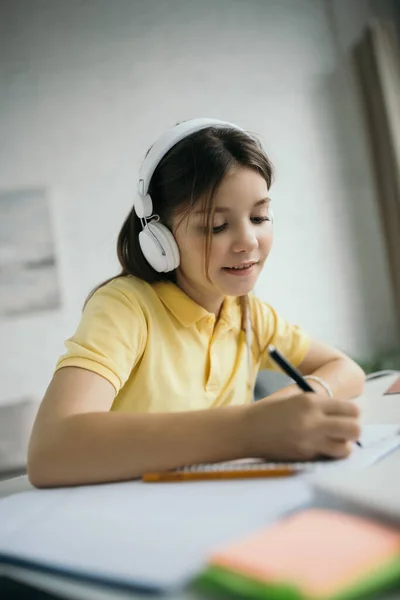 Menina positiva na escrita fones de ouvido enquanto aprende em casa — Fotografia de Stock