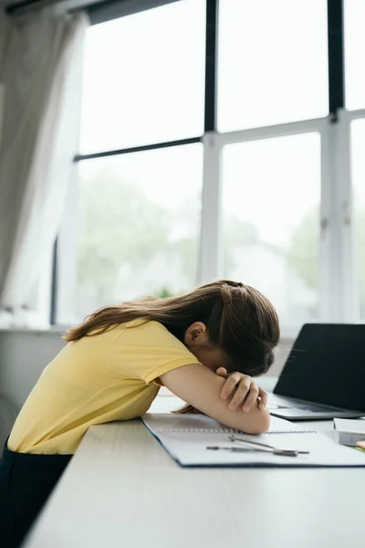 Side view of exhausted schoolgirl sleeping near laptop with blank screen on table — Stock Photo