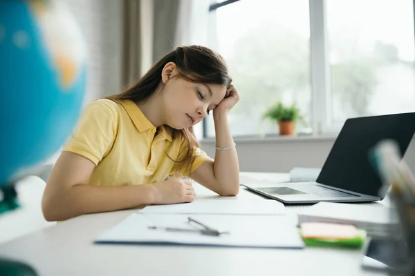 Tired girl with closed eyes sitting near laptop with blank screen at home on blurred foreground — Stock Photo