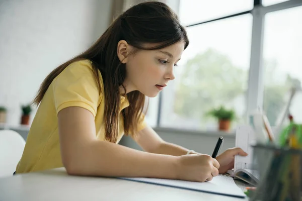 Брюнетка дівчина тримає ручку і дивиться в книгу під час навчання вдома — стокове фото