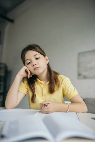 Pensoso e stanco ragazza che tiene penne mentre seduto con mano vicino al viso a casa — Foto stock