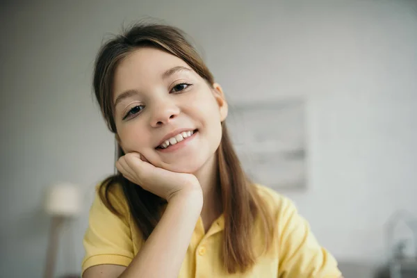 Portrait of brunette girl with hand near face smiling at camera on blurred background — Stock Photo