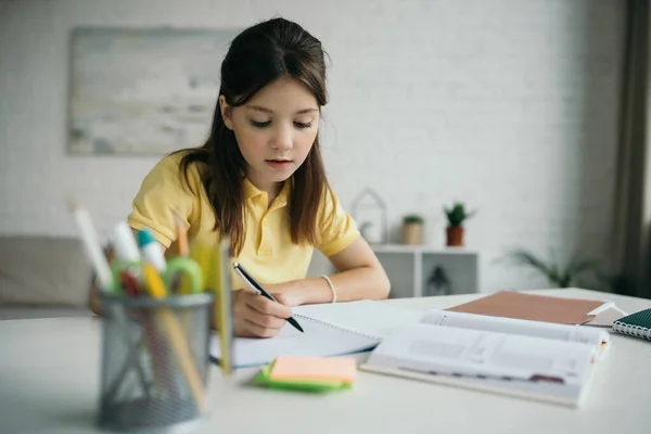 Брюнетка дівчина з ручкою, що пише в копіювальній книзі біля щоденника та канцелярських приладів на розмитому фоні — Stock Photo