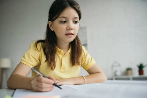 Вдумчивая девушка сидит с ручкой во время учебы дома — стоковое фото