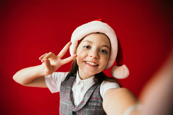 Happy girl showing victory sign while smiling at camera on blurred foreground isolated on red — Stock Photo