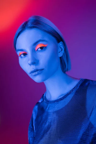 Young woman with glowing makeup in blue neon light on purple and coral background — Stock Photo