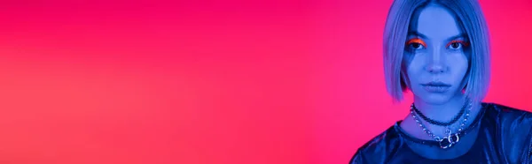 Ritratto di bella donna che guarda la macchina fotografica in luce blu al neon su sfondo corallo e rosa, banner — Foto stock