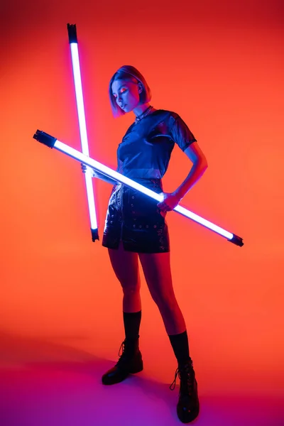 Volle Länge der jungen Frau mit leuchtenden Neonlampen auf korallenfarbenem und lila Hintergrund — Stockfoto