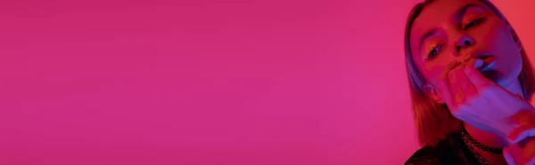 Donna con trucco al neon che tiene la mano vicino al viso su sfondo rosa scuro con spazio copia, banner — Foto stock