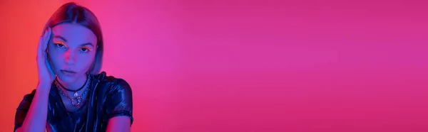 Portrait of young woman with bright neon makeup in blue neon light on coral and pink background, banner — Stock Photo