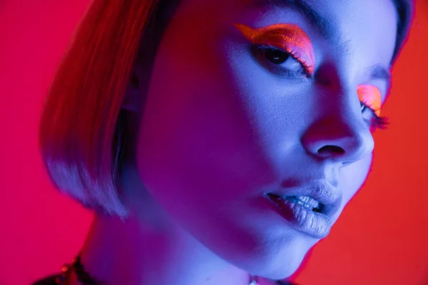 Nahaufnahme Porträt einer Frau mit leuchtendem Neon-Make-up auf rotem und rosa Hintergrund — Stockfoto