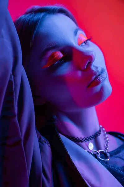 Porträt einer hübschen Frau mit Neon-Make-up, die im blauen Licht auf rotem und rosa Hintergrund wegschaut — Stockfoto