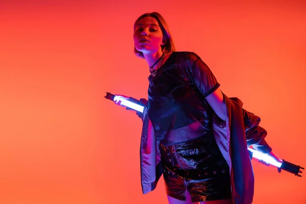 Модна жінка зі світиться неоновою лампою, дивлячись на камеру ізольована на кораловому червоному — стокове фото