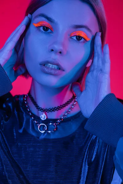 Portrait of woman with glowing neon makeup holding hands near face in blue light on deep pink background — Stock Photo