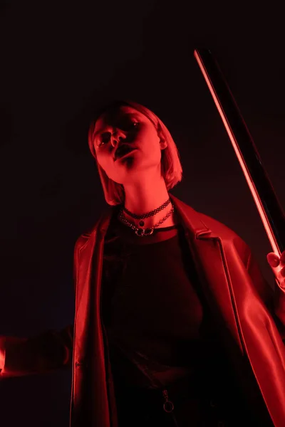 Низкий угол зрения женщины, держащей неоновую лампу с красным светом на черном фоне — стоковое фото
