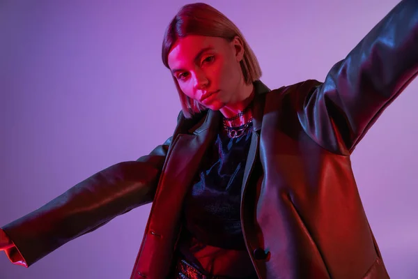 Femme élégante en veste en cuir posant avec les mains tendues isolées sur violet — Photo de stock