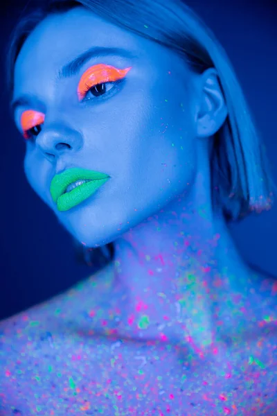 Retrato de mulher jovem com maquiagem fluorescente e tinta de néon no corpo isolado em azul escuro — Fotografia de Stock