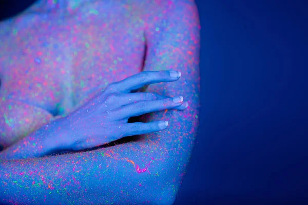 Visão parcial da mulher com manchas de néon brilhante no corpo isolado em azul escuro — Fotografia de Stock