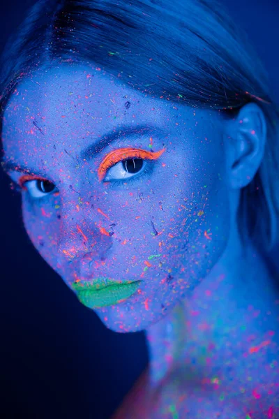 Retrato de mujer con maquillaje de neón y pintura fluorescente en la cara aislada en azul oscuro - foto de stock