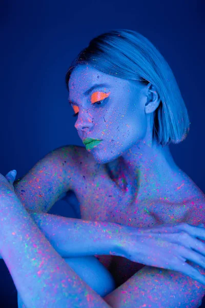 Nackte Frau mit Neon-Make-up und Körper in fluoreszierender Farbe isoliert auf dunkelblau — Stockfoto