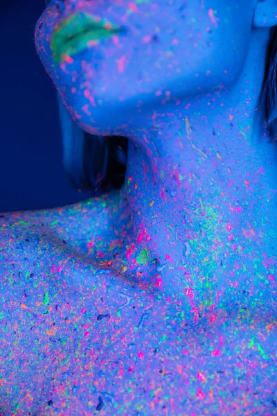 Vista parcial de la mujer joven en colorido cuerpo de neón pintura aislada en azul oscuro - foto de stock
