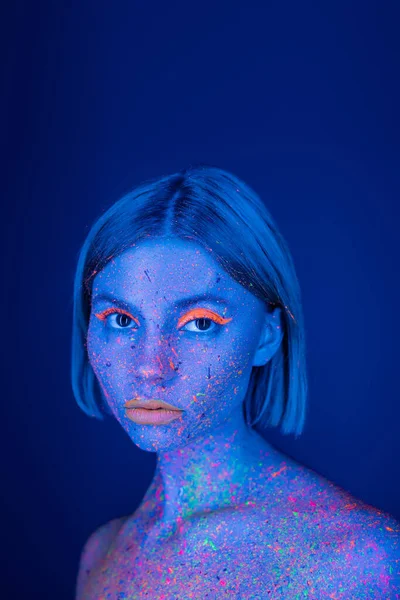 Retrato de mulher com maquiagem brilhante e manchas de tinta de néon no corpo isolado em azul escuro — Fotografia de Stock