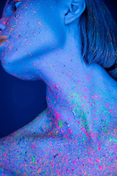Nahaufnahme einer Frau mit bunter Neonfarbe auf dem Körper, die isoliert auf dunkelblauem Grund posiert — Stockfoto
