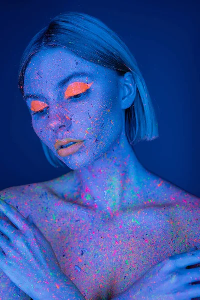 Nude woman in bright neon makeup and fluorescent paint splatters posing isolated on dark blue — Stock Photo