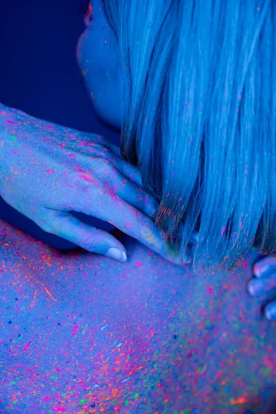 Vue partielle de la femme touchant le corps coloré avec une peinture au néon brillante isolée sur bleu foncé — Photo de stock