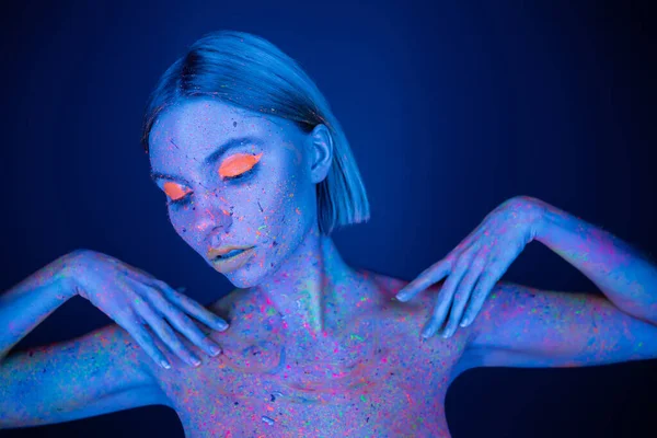 Hübsche Frau in hellem Make-up und leuchtender Neon-Körperfarbe posiert isoliert auf dunkelblau — Stockfoto