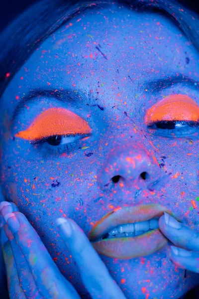 Portrait en gros plan d'une femme au maquillage fluorescent touchant le visage en néon bleu — Photo de stock