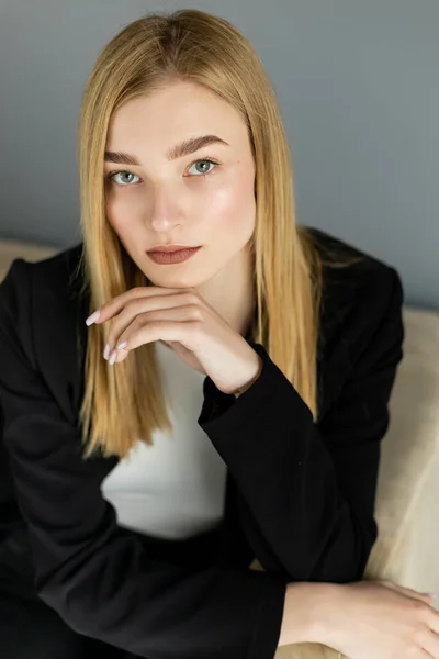 Portrait of young blonde woman looking at camera while sitting on blurred couch — Stock Photo