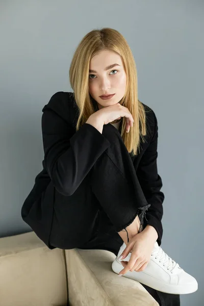 Ritratto di giovane donna in jeans neri e giacca in posa sul divano di casa — Foto stock