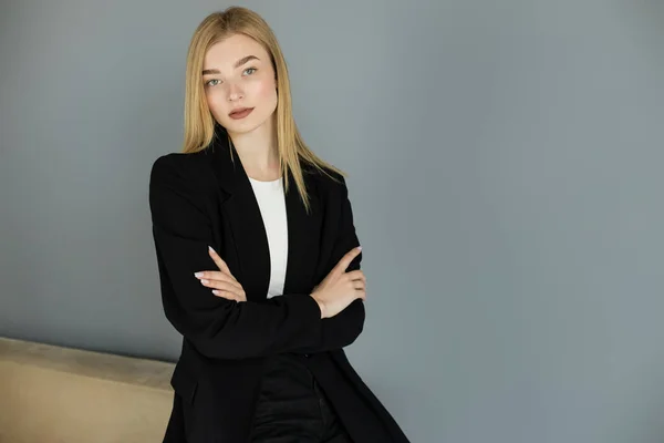Confident woman in black jacket crossing arms near couch at home — Stock Photo