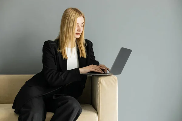 Treinador loiro em casaco preto usando laptop no sofá em casa — Fotografia de Stock