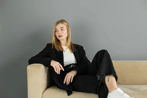 Bella donna in giacca guardando lontano mentre seduto sul divano a casa — Foto stock