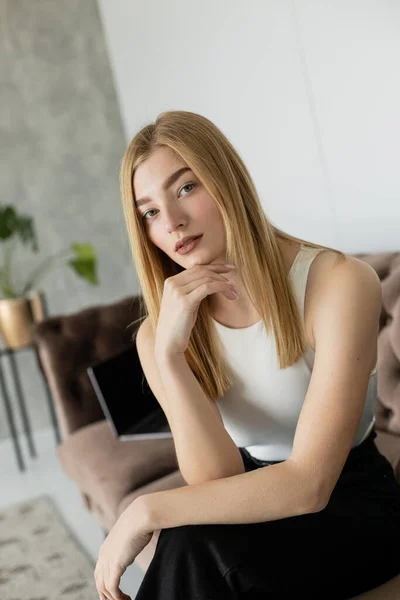 Портрет молодої жінки, дивлячись на камеру, сидячи на розмитому дивані вдома — стокове фото