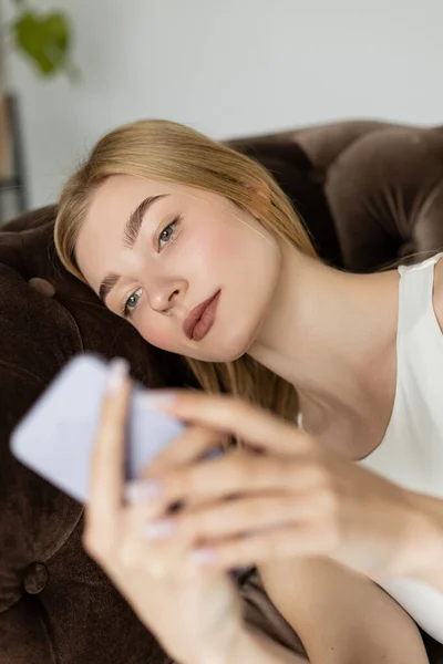 Porträt einer jungen Frau in Top mit verschwommenem Handy auf bequemer Couch — Stockfoto