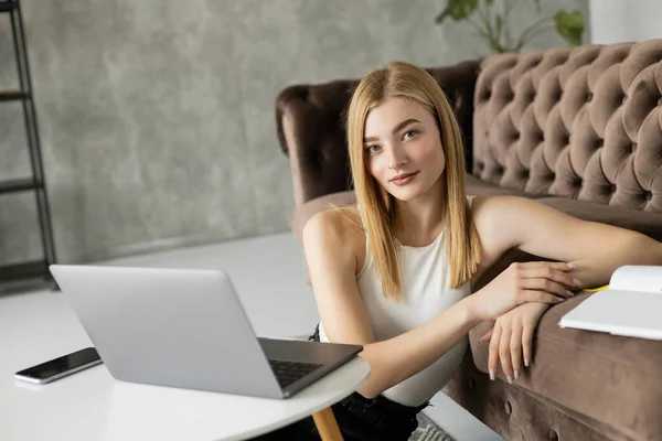 Young coach looking at camera near devices and notebook at home — Stock Photo