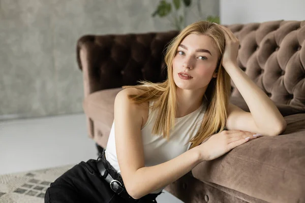 Portrait de jeune femme blonde regardant la caméra près du canapé à la maison — Photo de stock