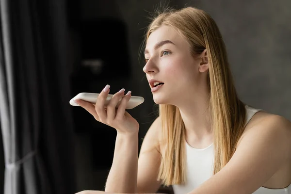 Donna bionda che registra il messaggio vocale sullo smartphone a casa — Foto stock