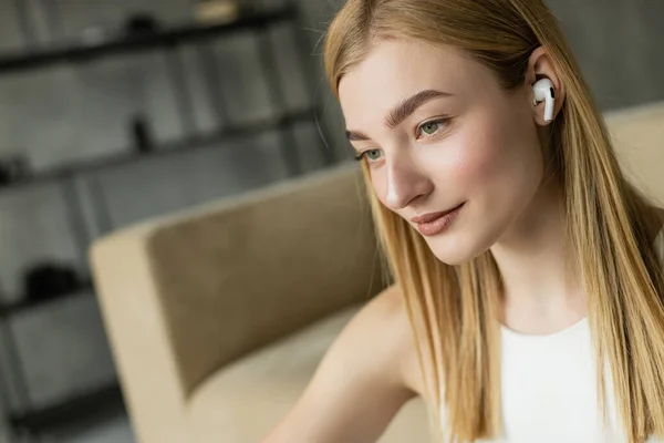 Pretty blonde woman listening music in wireless earphone at home — Stock Photo