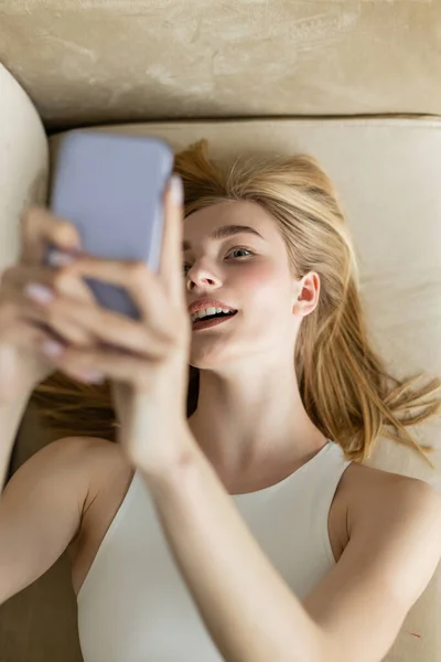 Top view of young woman with opened mouth taking selfie on smartphone on couch — Stock Photo