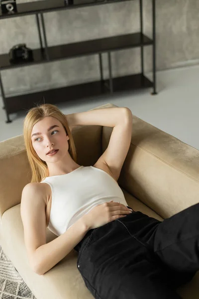 Jovem mulher em cima e jeans deitado no sofá bege em casa — Fotografia de Stock