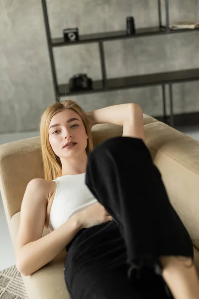 Jolie jeune femme en haut et jeans regardant la caméra tout en étant couché sur le canapé à la maison — Photo de stock