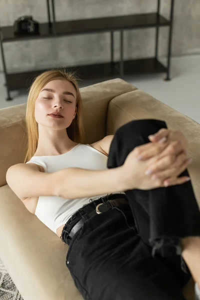 Mulher loira em cima e jeans relaxando no sofá bege em casa — Fotografia de Stock