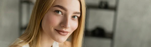 Jeune femme blonde souriant à la caméra dans le salon flou, bannière — Photo de stock